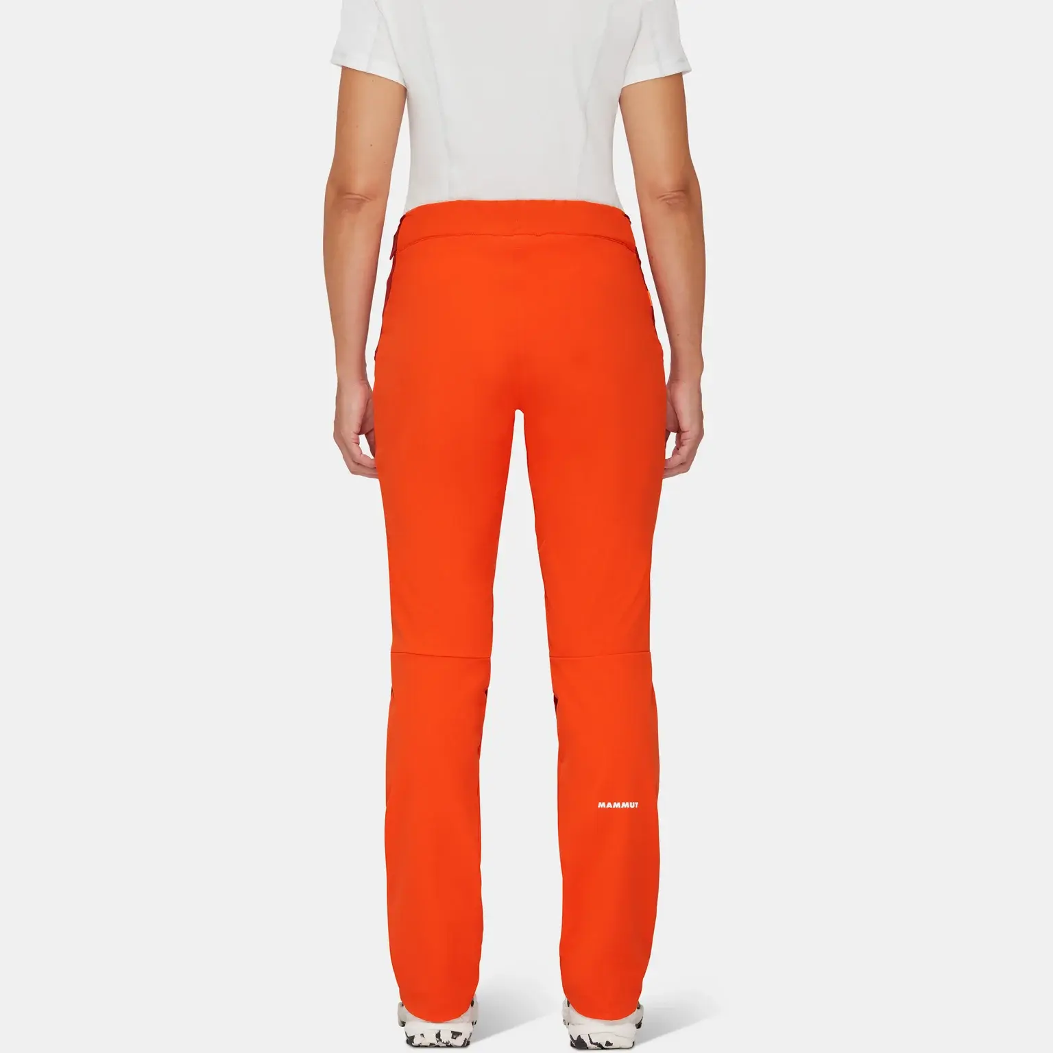 Person wearing a Mammut white shirt and bright orange Mammut outdoor pants stands facing away, showcasing the back view of the mountaineering outfit.