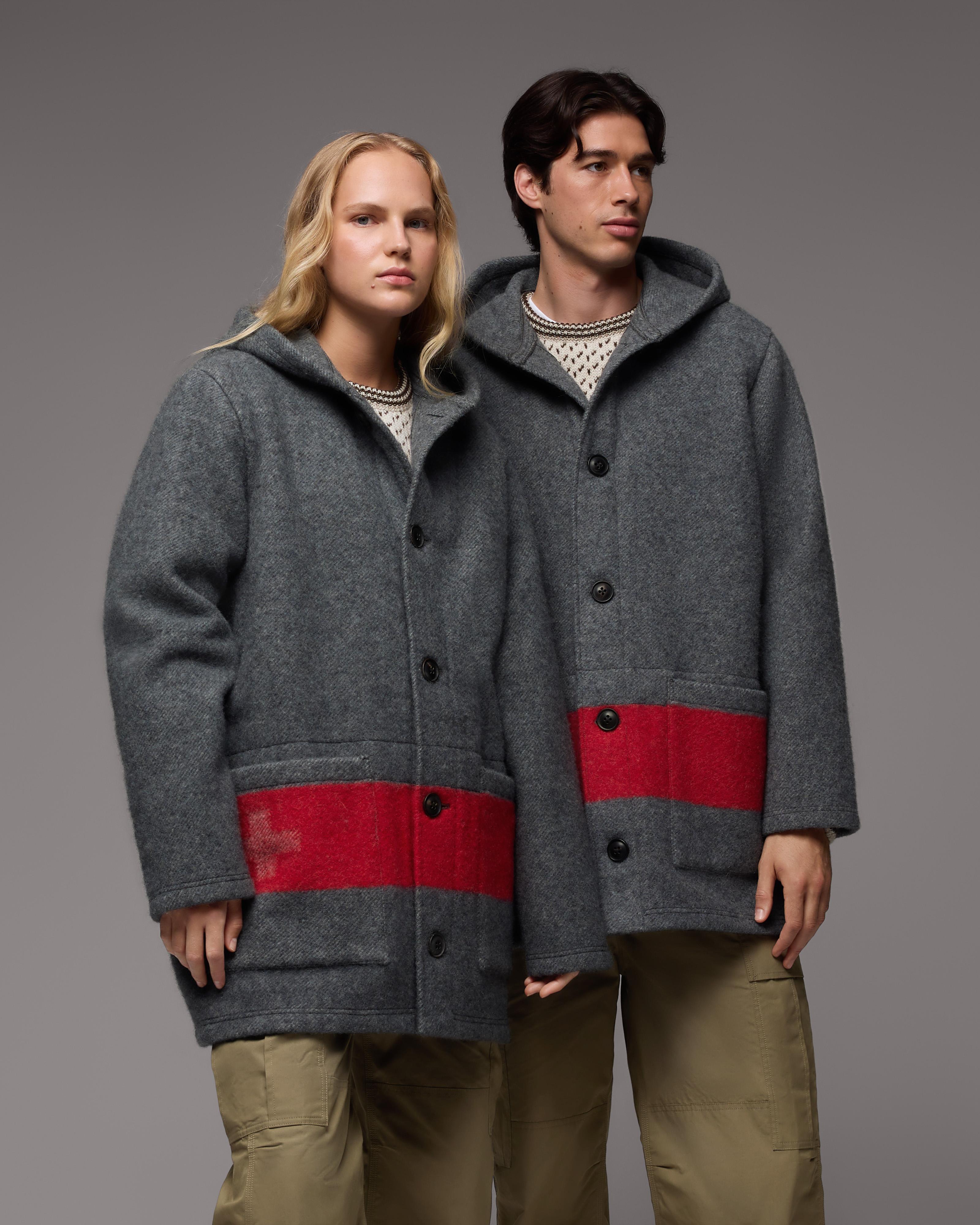 Two people in Mammut gray hooded jackets with red stripes and khaki pants stand side by side against a plain gray backdrop.