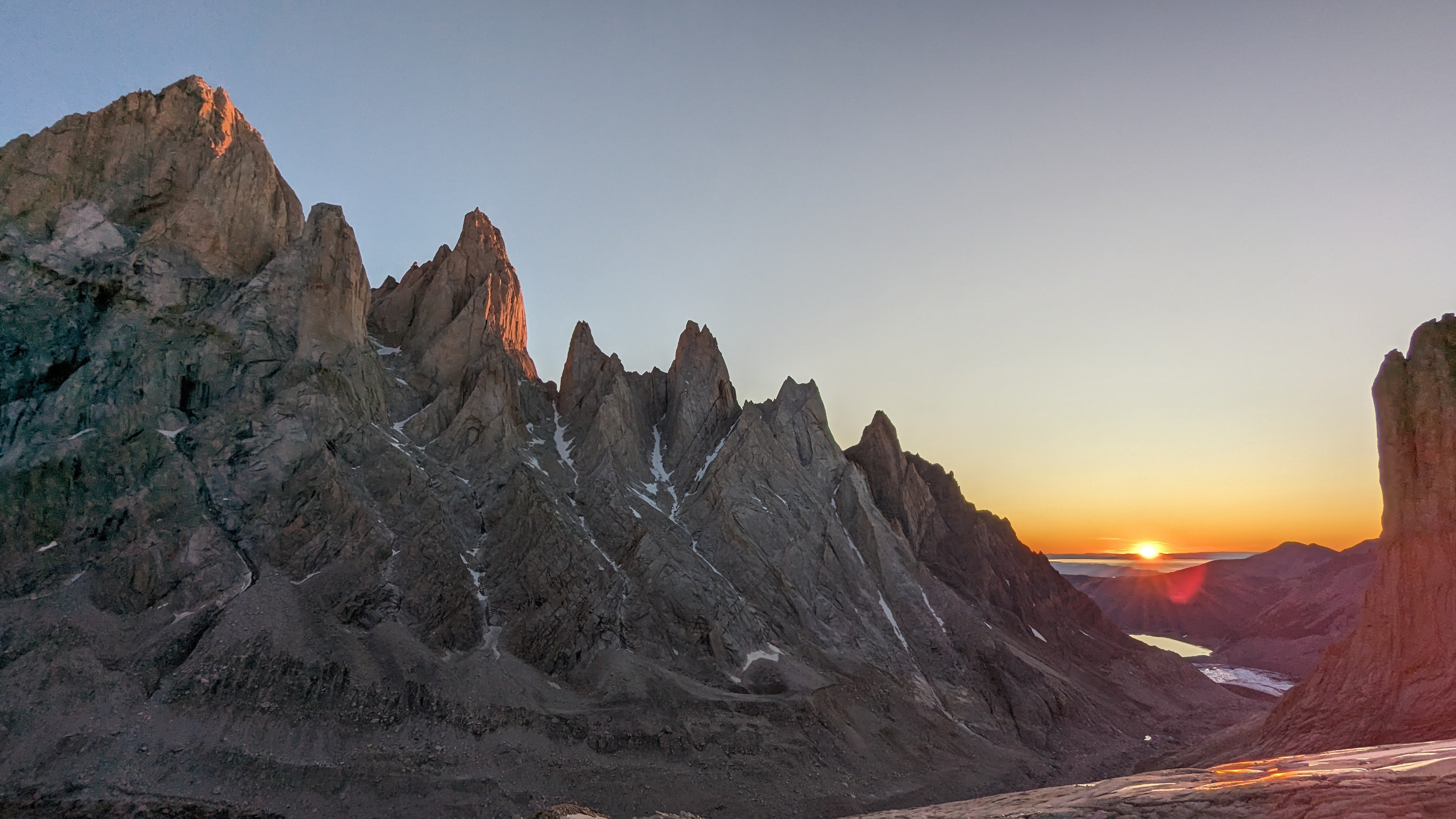 Sunrise over rugged mountain peaks with a small lake in the distance under a clear sky, ideal for Mammut mountaineering adventures.